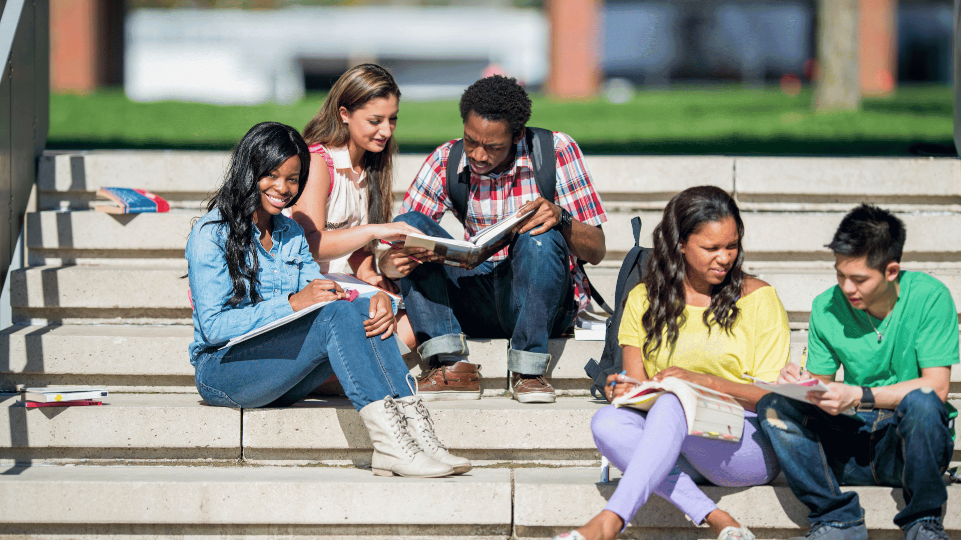 Students studying together on outdoor steps, sharing books and notes.