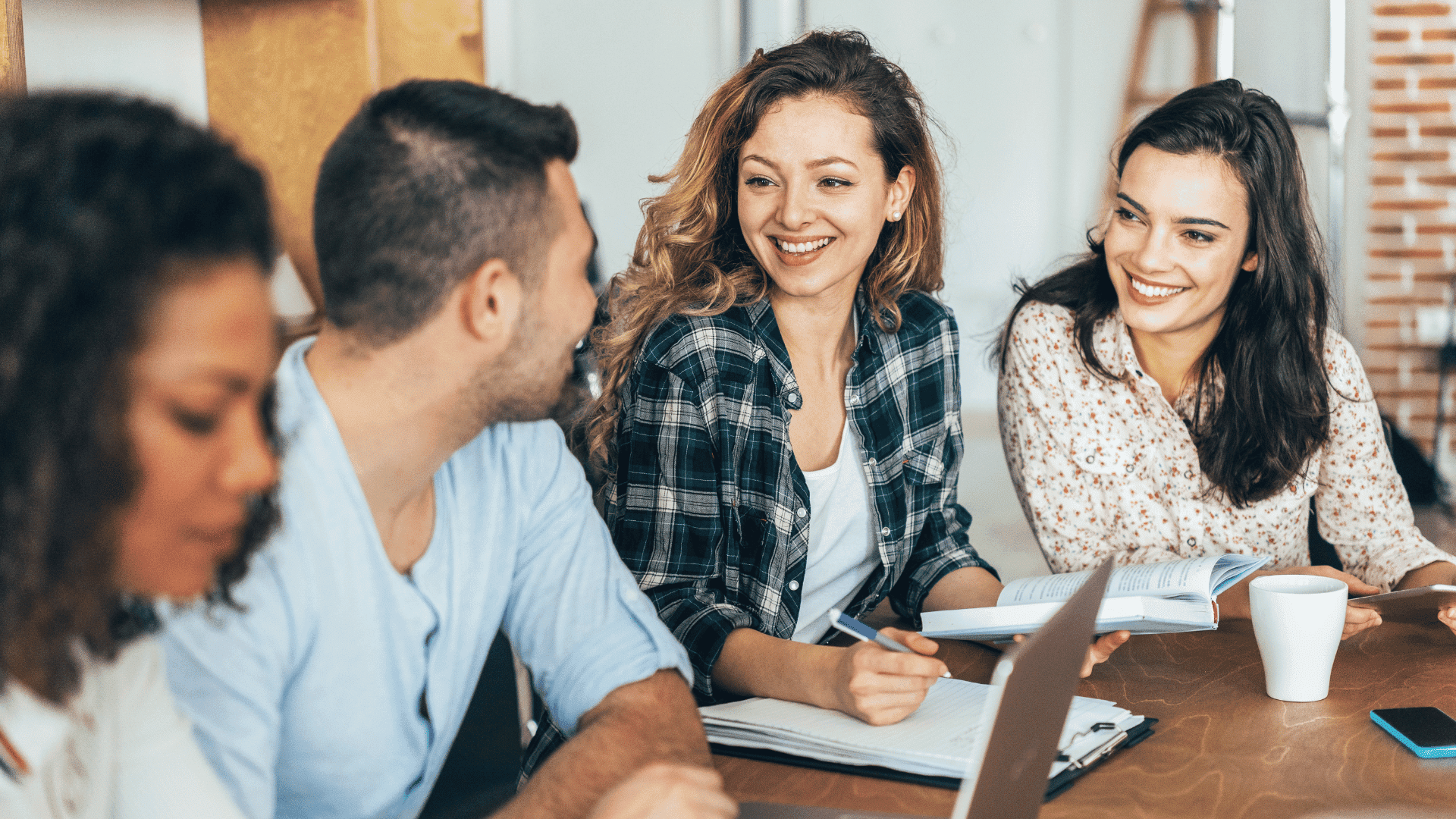 Group of people smiling and talking at a table, with notebooks and a laptop.